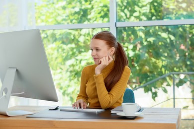 Photo of Teenage girl using computer at wooden desk indoors. Home workplace