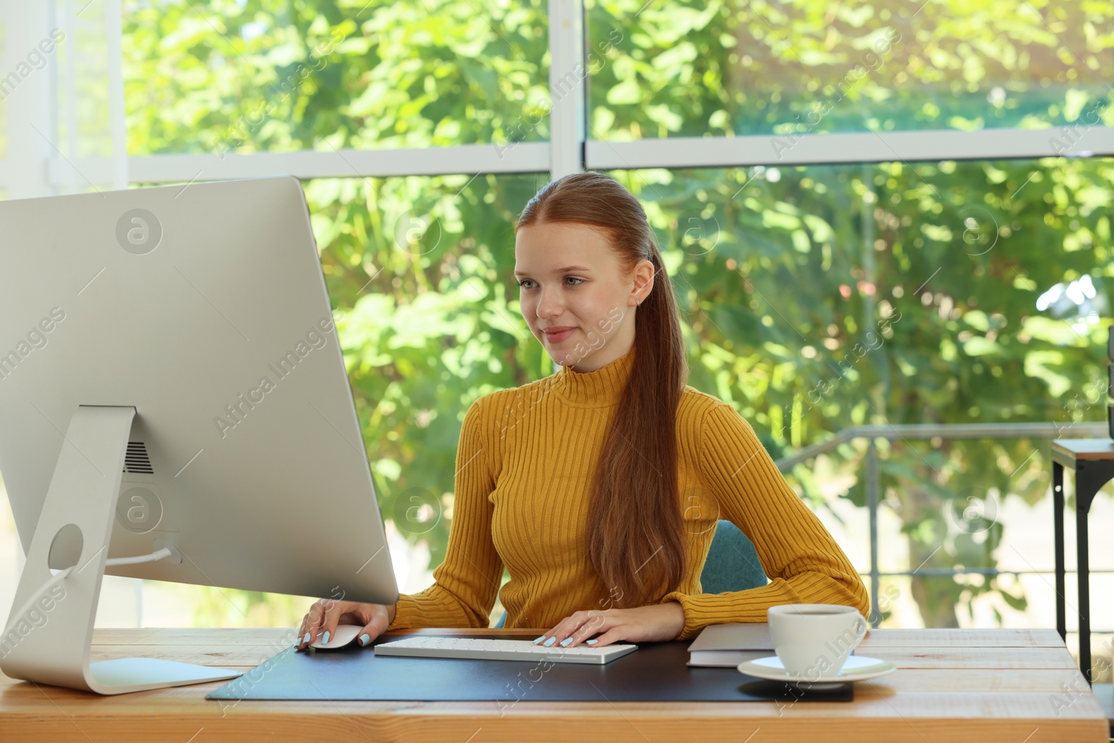 Photo of Teenage girl using computer at wooden desk indoors. Home workplace