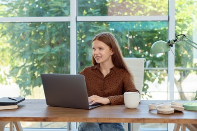 Photo of Teenage girl using laptop at wooden desk indoors. Home workplace