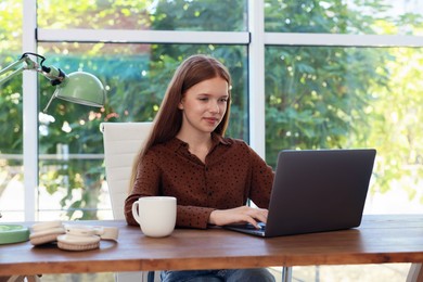 Photo of Teenage girl using laptop at wooden desk indoors. Home workplace