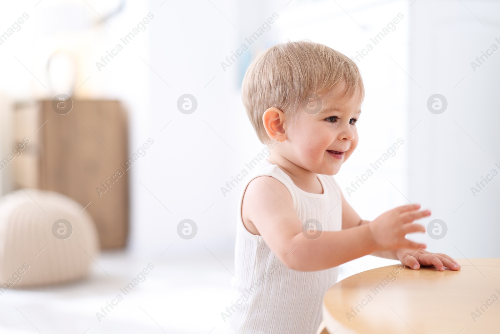 Cute little baby near table at home, space for text Photo of Cute little baby near table at home, space for text
