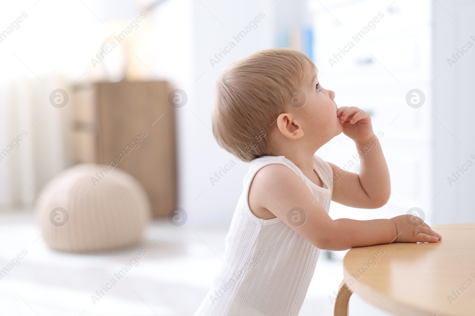 Cute little baby near table at home, space for text Photo of Cute little baby near table at home, space for text