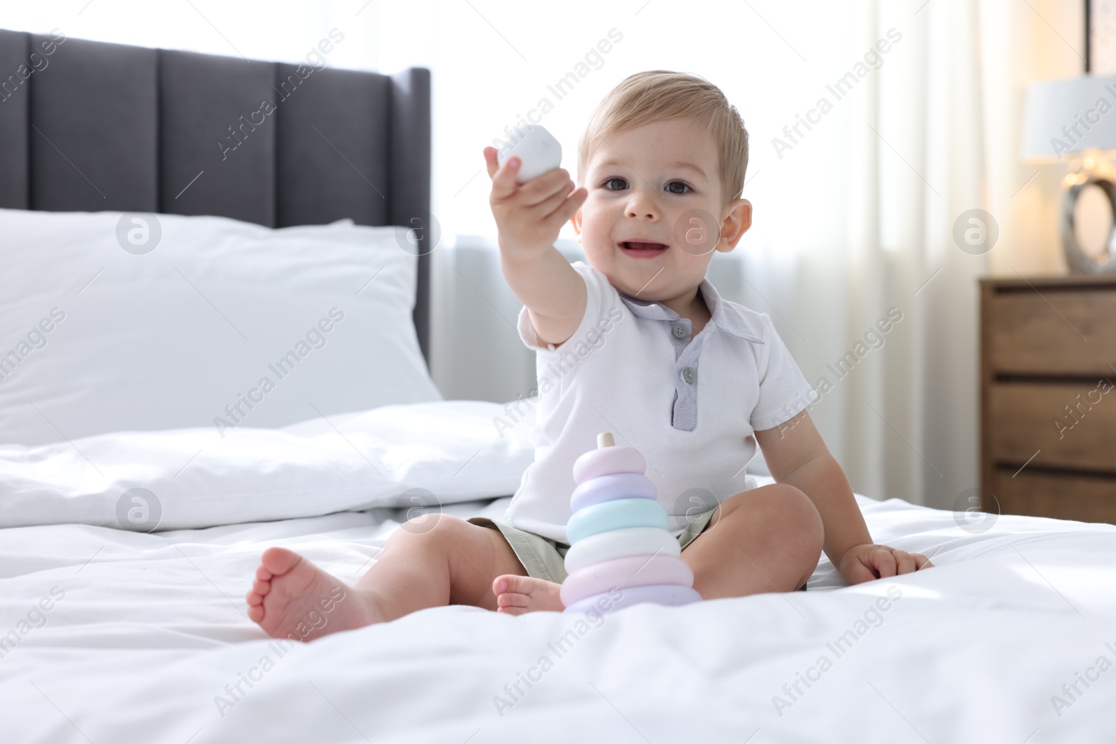 Photo of Cute little baby playing with toy pyramid on bed at home