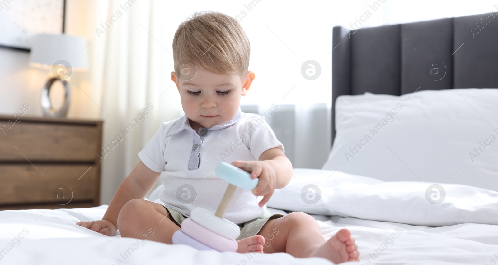 Photo of Cute little baby playing with toy pyramid on bed at home