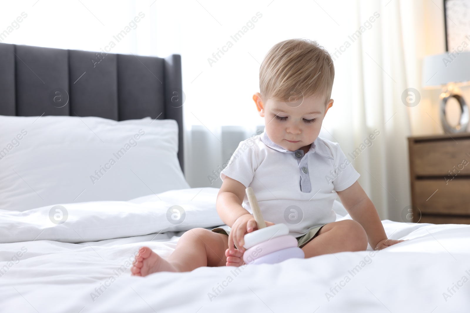 Photo of Cute little baby playing with toy pyramid on bed at home, space for text