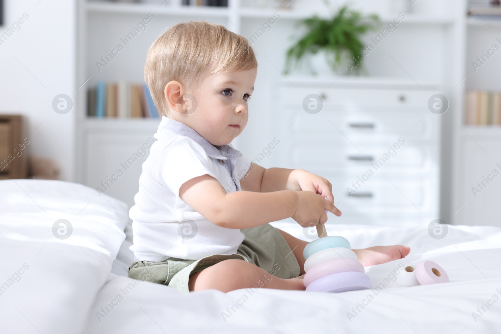 Photo of Cute little baby playing with toy pyramid on bed at home
