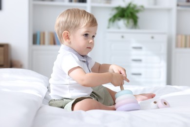 Photo of Cute little baby playing with toy pyramid on bed at home