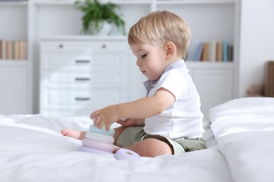 Photo of Cute little baby playing with toy pyramid on bed at home