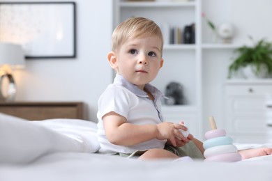 Photo of Cute little baby playing with toy pyramid on bed at home
