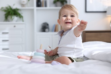 Photo of Cute little baby playing with toy pyramid on bed at home
