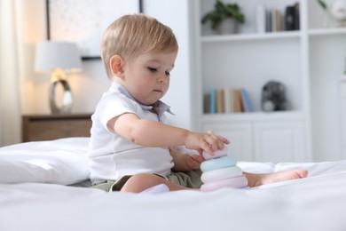 Photo of Cute little baby playing with toy pyramid on bed at home
