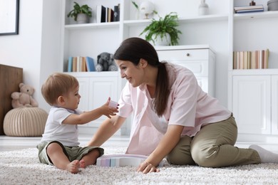 Photo of Mother and her cute little baby playing with toy on floor at home