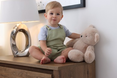 Photo of Cute little baby and toy on wooden dresser indoors