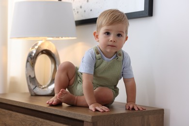 Photo of Cute little baby and toy on wooden dresser indoors