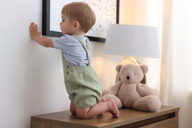 Photo of Cute little baby and toy on wooden dresser indoors