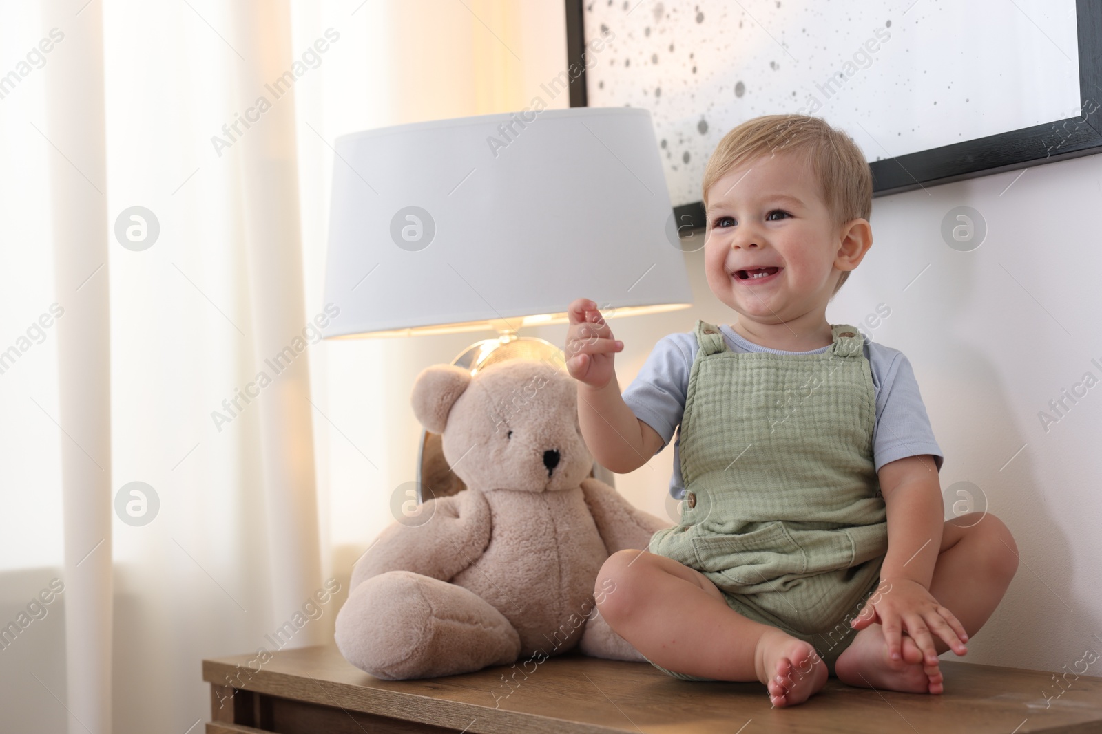 Cute little baby and toy on wooden dresser indoors, space for text Photo of Cute little baby and toy on wooden dresser indoors, space for text