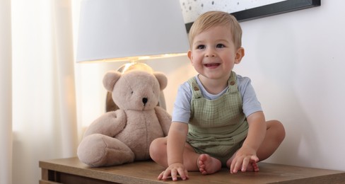 Photo of Cute little baby and toy on wooden dresser indoors