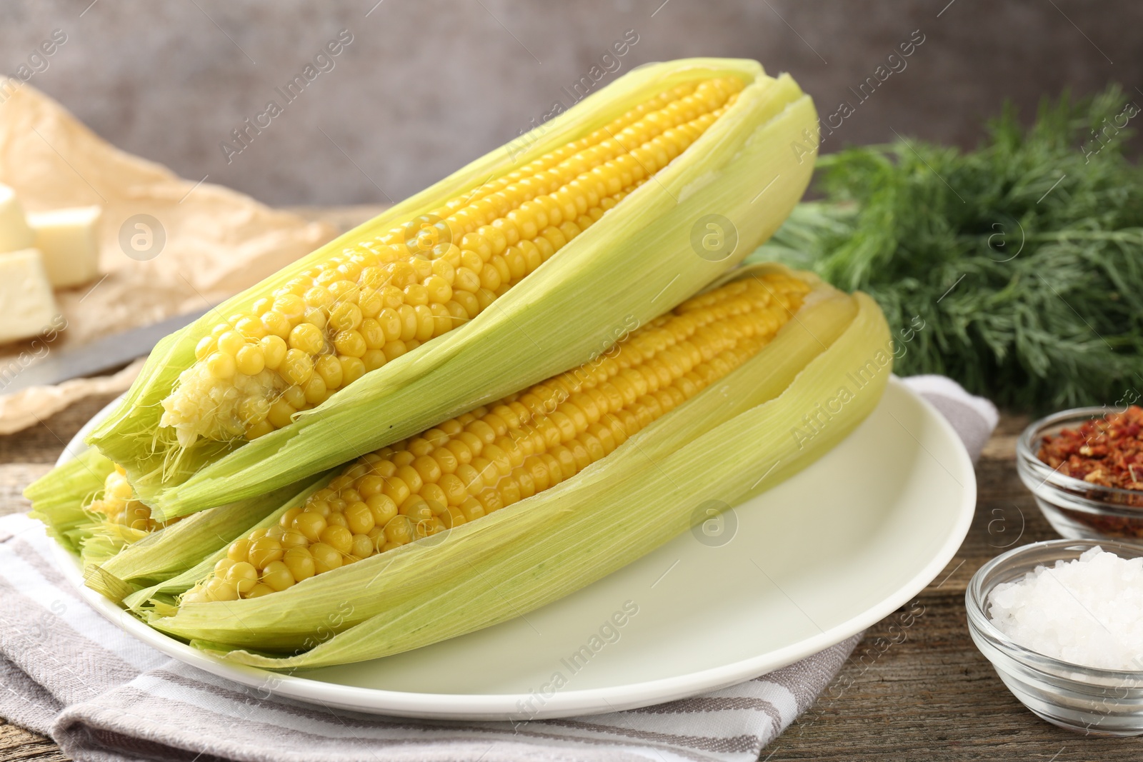 Tasty boiled corncobs, dill and spices on wooden table, closeup Photo of Tasty boiled corncobs, dill and spices on wooden table, closeup