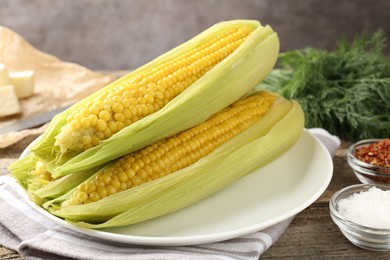 Photo of Tasty boiled corncobs, dill and spices on wooden table, closeup