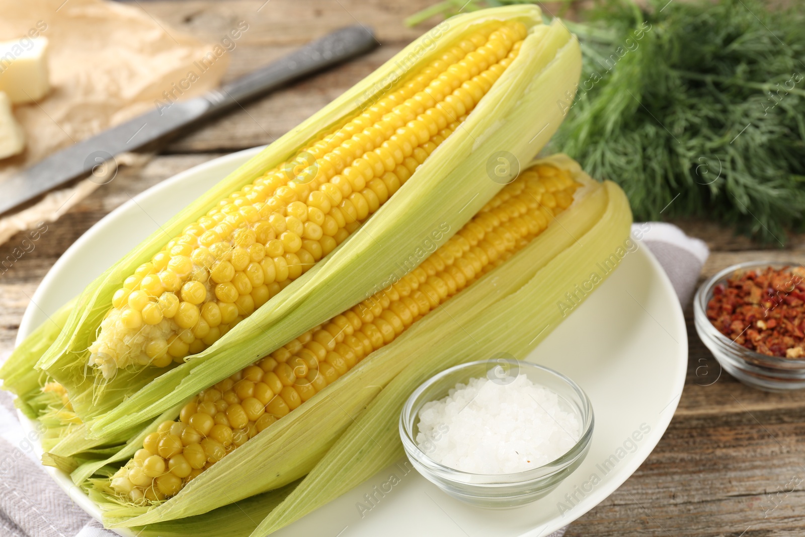 Photo of Tasty boiled corncobs, dill and spices on wooden table, closeup