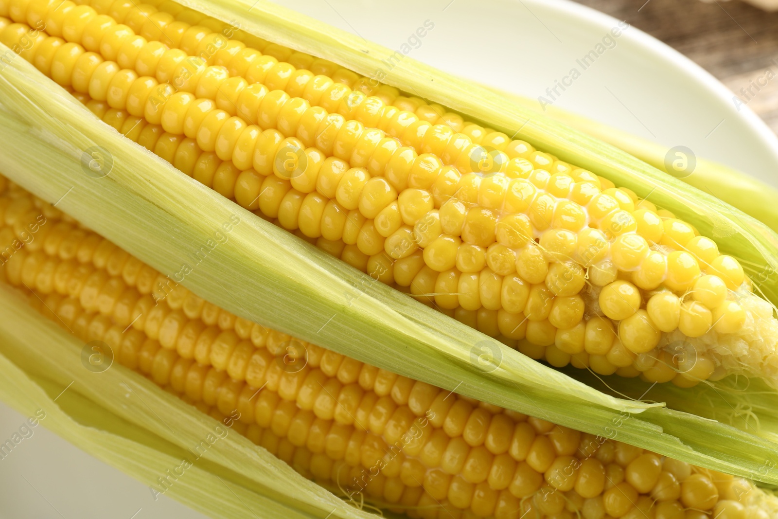 Tasty boiled corncobs with leaves on table, closeup Photo of Tasty boiled corncobs with leaves on table, closeup