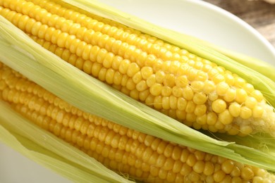 Photo of Tasty boiled corncobs with leaves on table, closeup