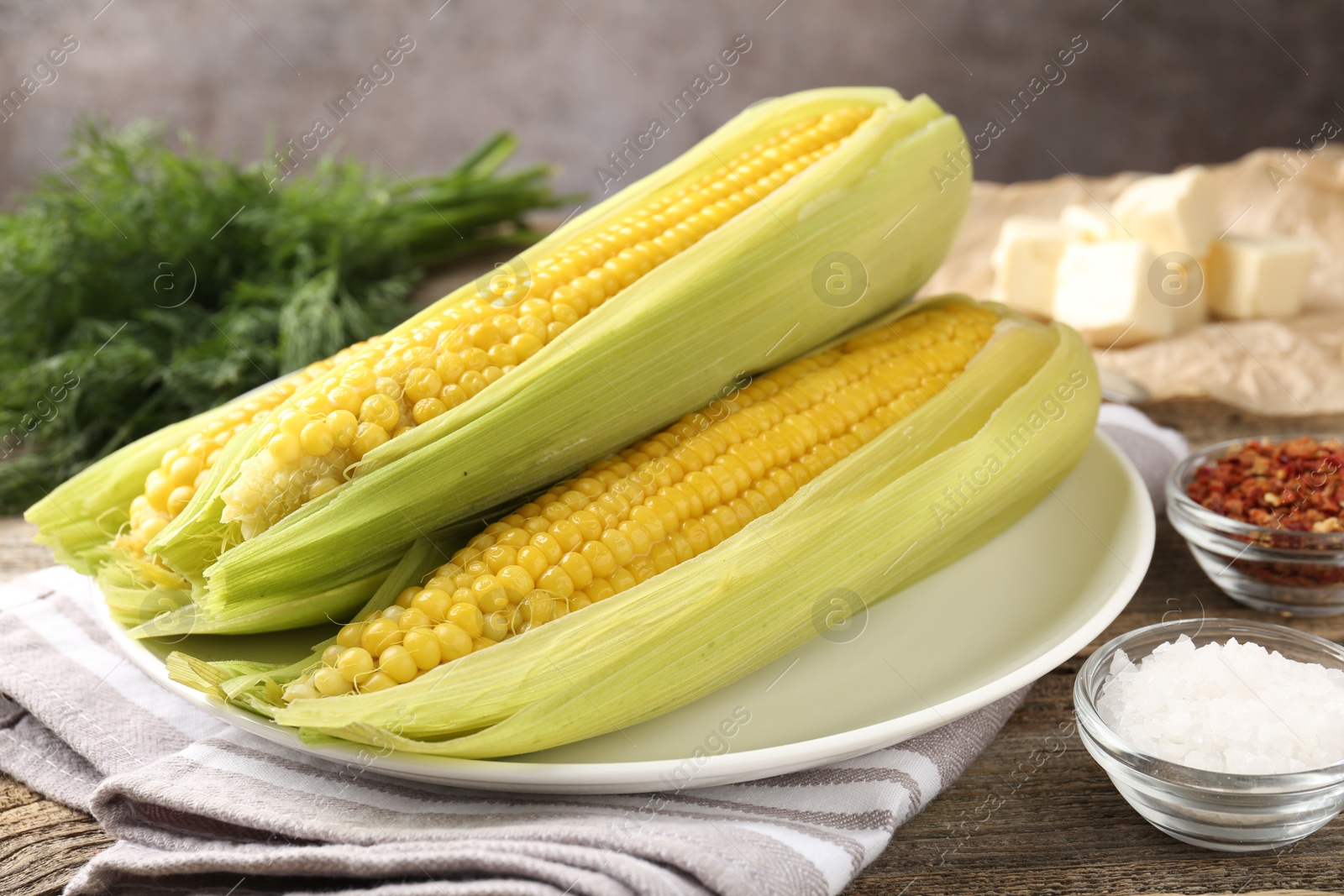 Photo of Tasty boiled corncobs, dill and spices on wooden table, closeup