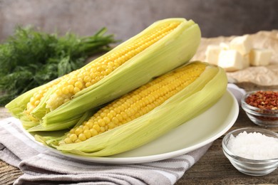 Photo of Tasty boiled corncobs, dill and spices on wooden table, closeup