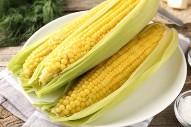 Photo of Tasty boiled corncobs on wooden table, closeup