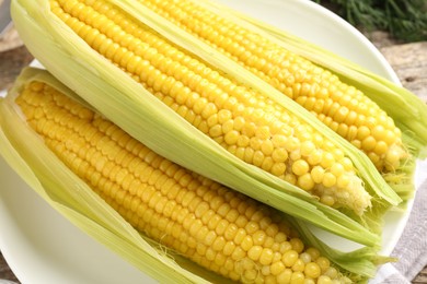 Photo of Tasty boiled corncobs on wooden table, closeup
