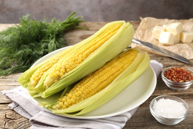 Photo of Tasty boiled corncobs, dill and spices on wooden table, closeup