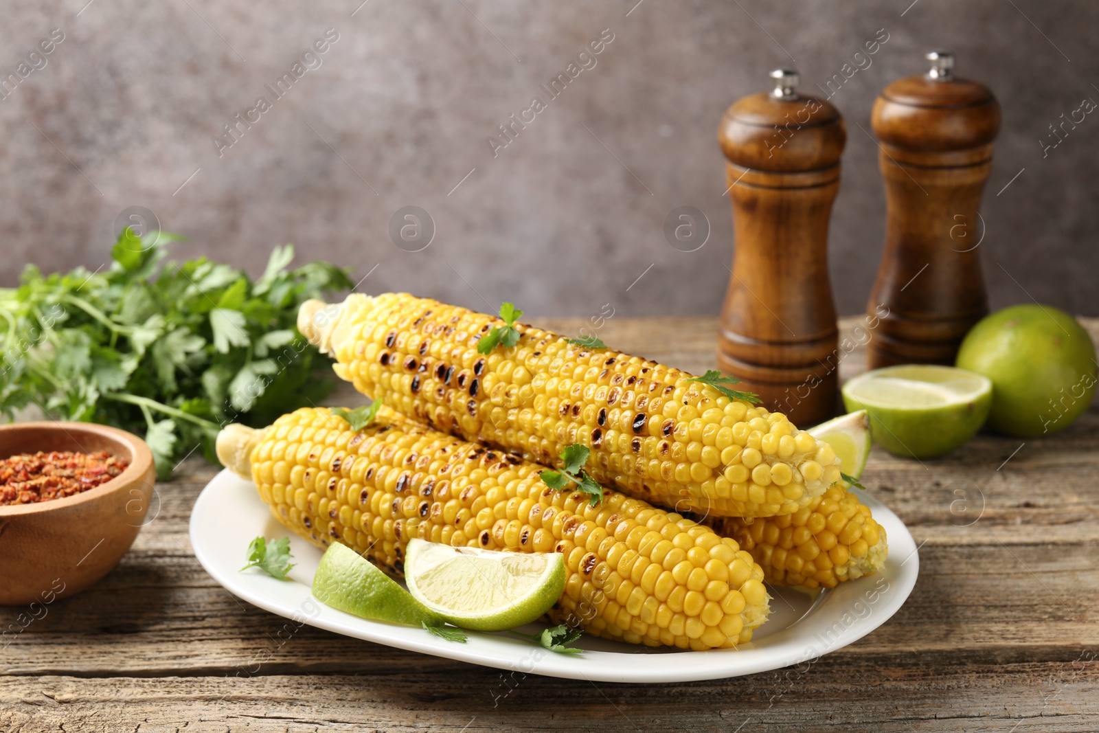 Tasty grilled corncobs with parsley and lime slices on wooden table Photo of Tasty grilled corncobs with parsley and lime slices on wooden table