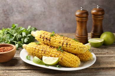 Photo of Tasty grilled corncobs with parsley and lime slices on wooden table