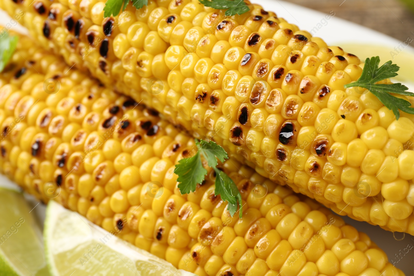 Tasty grilled corncobs with parsley and lime slices on table, closeup Photo of Tasty grilled corncobs with parsley and lime slices on table, closeup