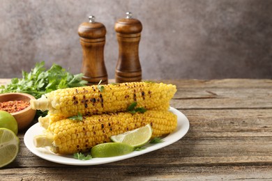 Photo of Tasty grilled corncobs with parsley and lime slices on wooden table. Space for text