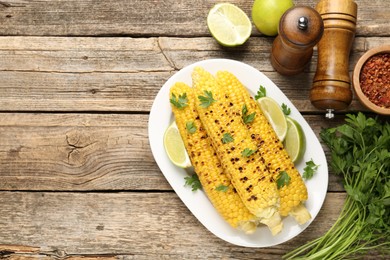 Photo of Tasty grilled corncobs with parsley and lime slices on wooden table, flat lay. Space for text