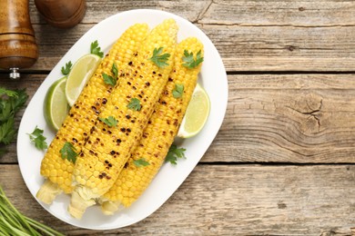 Photo of Tasty grilled corncobs with parsley and lime slices on wooden table, flat lay. Space for text