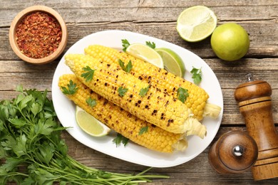 Photo of Tasty grilled corncobs with parsley and lime slices on wooden table, flat lay