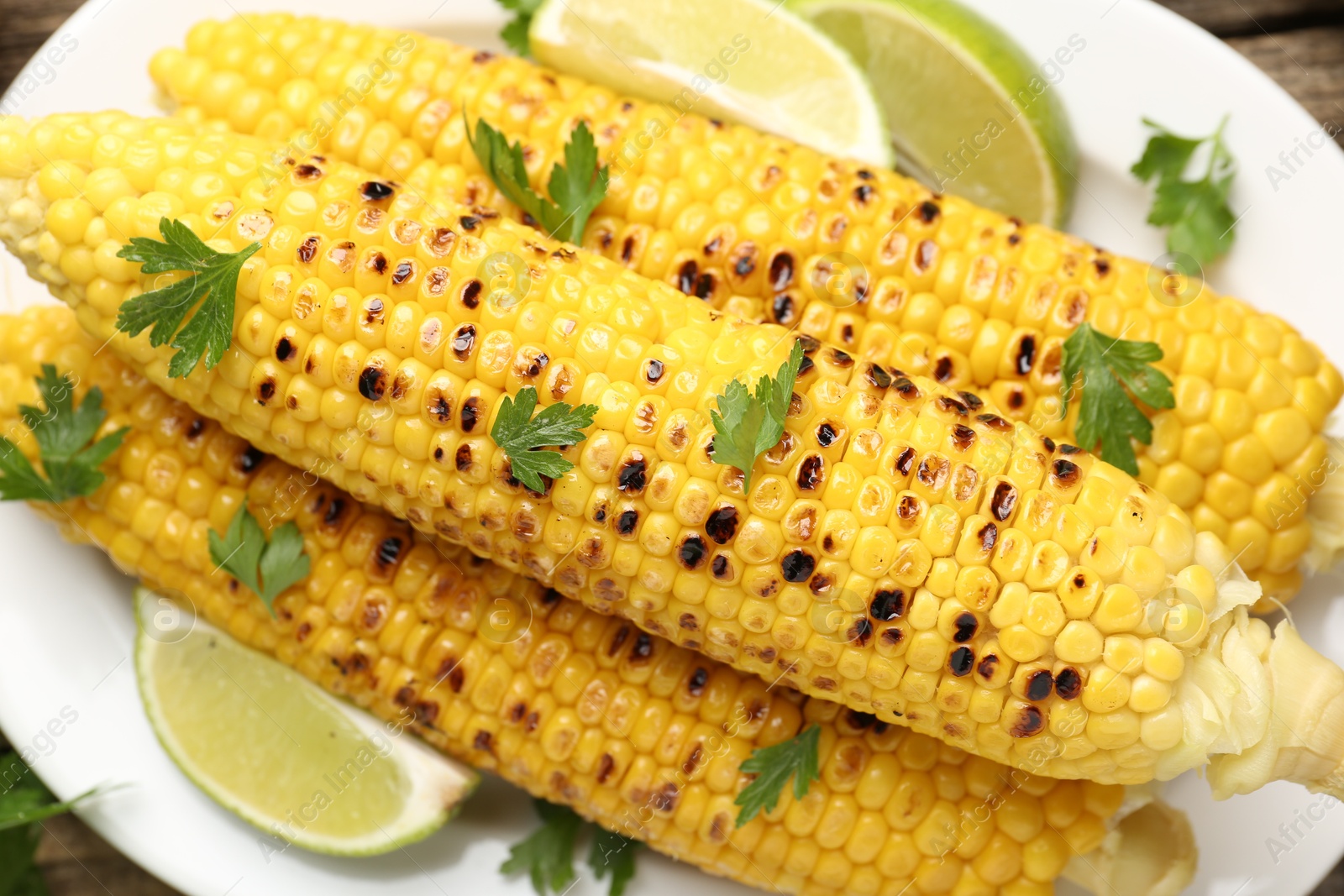 Photo of Tasty grilled corncobs with parsley and lime slices on table, closeup