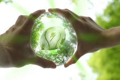 Image of Electricity and nature. Man holding crystal ball with light bulb and lightning symbol inside outdoors, closeup