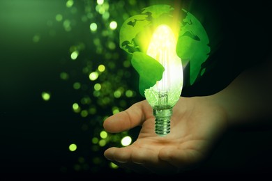 Image of Electricity and nature. Man holding globe with glowing light bulb inside against green gradient background, closeup