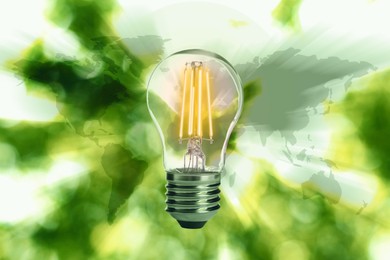 Image of Electricity and nature. Glowing light bulb and world map against blurred green background