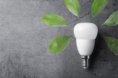 Image of Electricity and nature. Light bulb surrounded by green leaves on grey textured background, top view