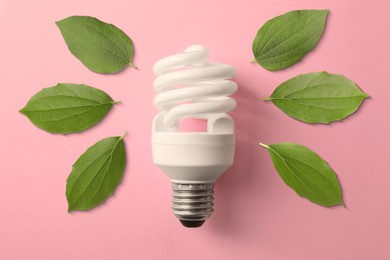 Image of Electricity and nature. Light bulb surrounded by green leaves on pink background, top view