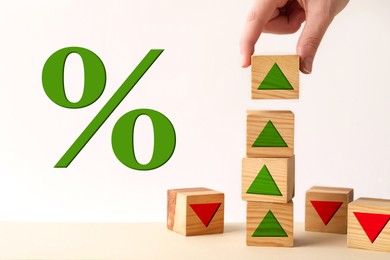 Image of Woman stacking wooden cubes with green arrows at table, closeup. Percent sign against white background