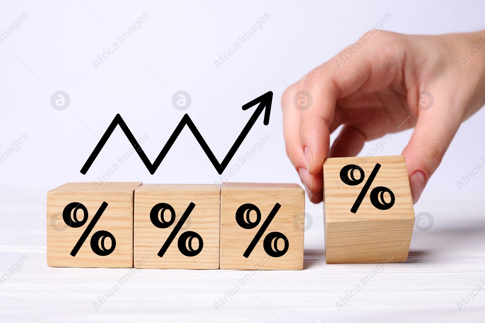 Image of Man holding wooden cube with percent sign at white table, closeup