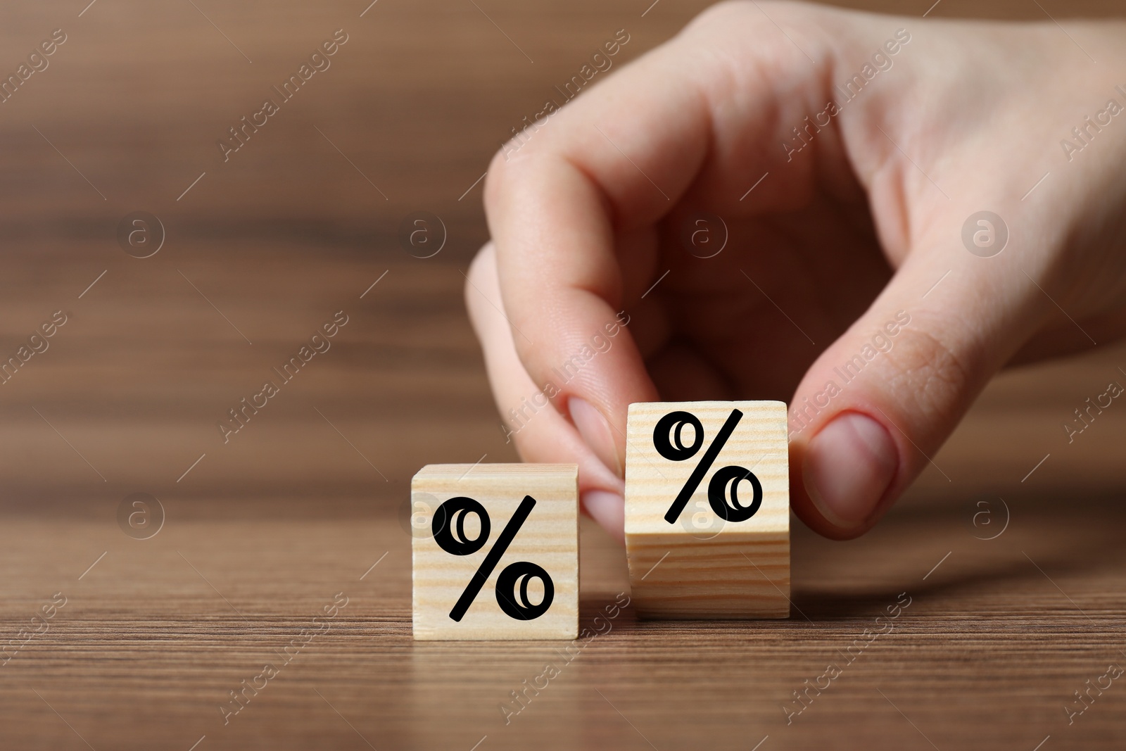 Image of Man holding wooden cube with percent sign at table, closeup
