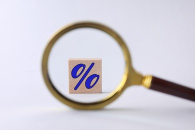 Image of Percent sign on wooden cubes against light background, view through magnifying glass