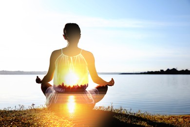 Image of Practicing yoga in nature. Woman meditating in lotus position on river shore. Double exposure with landscape at sunset
