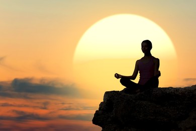 Image of Practicing yoga in nature. Woman meditating in lotus position on cliff against sunset sun in sky